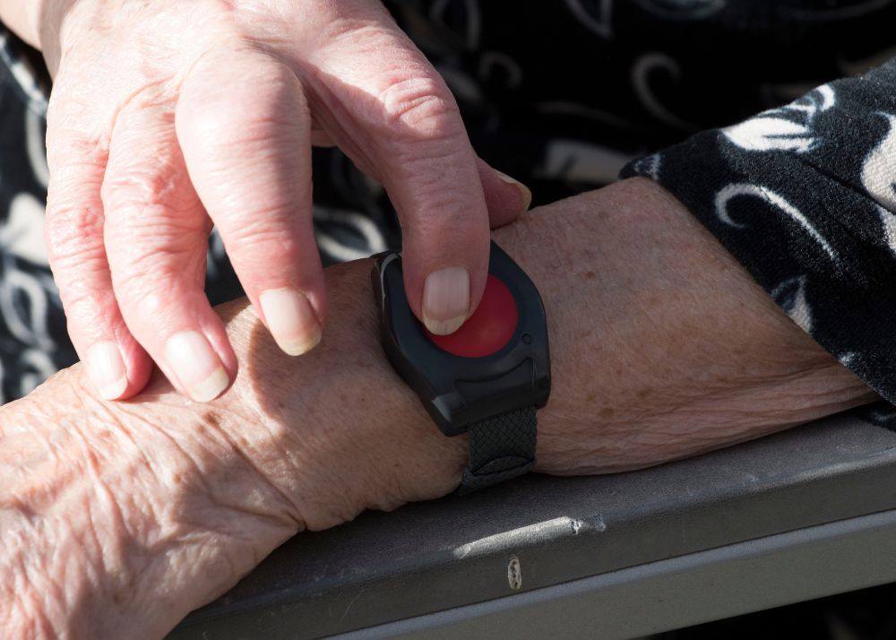 Displayed is a wrist with a medical alert armband and another hand pressing the red alert button.