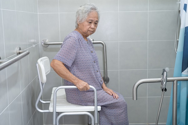 Displayed is an older woman using a shower stool with backrest and grab bar to safely stand up.