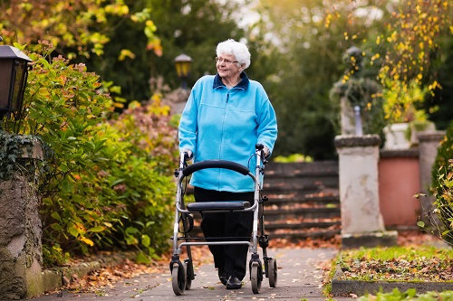 Displayed is an older woman taking a walk through a park in autumn with the help of her walker.