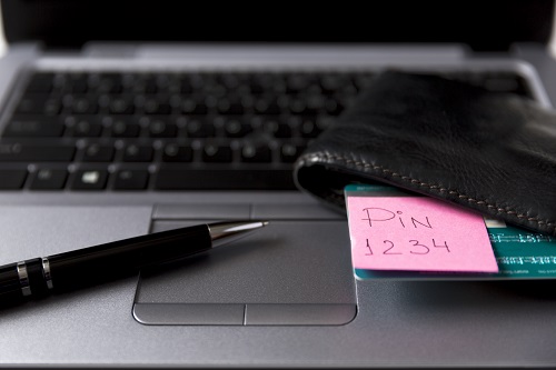  Displayed is a laptop keyboard with a pen and wallet placed on it. Out of the wallet peaks, a credit card and post-it note with the message Pin 1234.